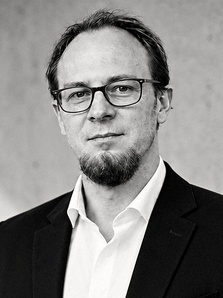 Porträt von Nicolas Weiß, Geschäftsführer von surge, in Anzug und weißem Hemd vor einer Betonwand